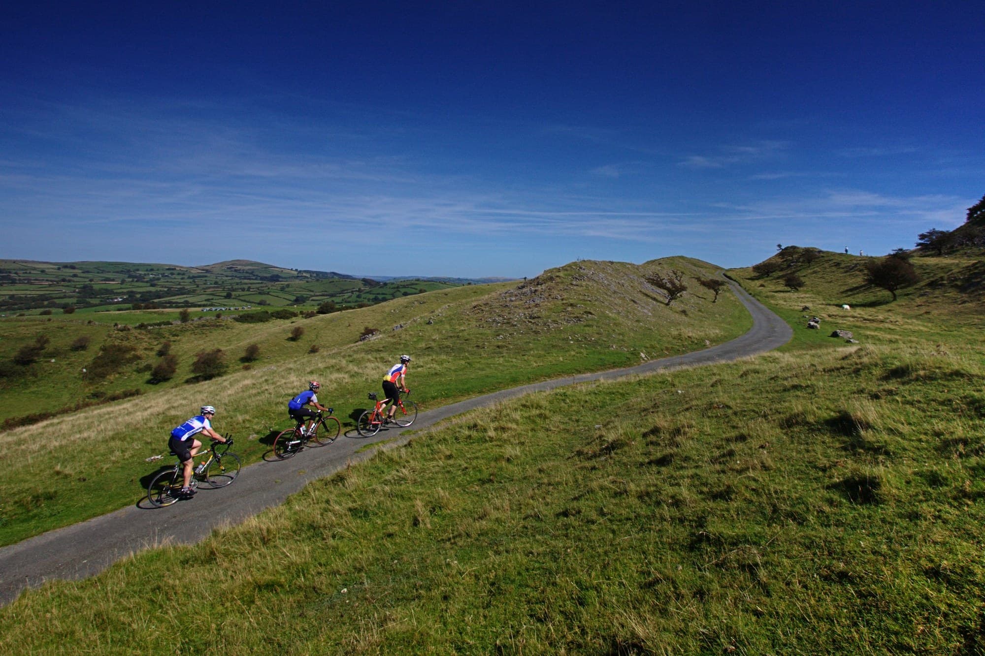 Three cyclists riding a lane over green hills in Wales.
