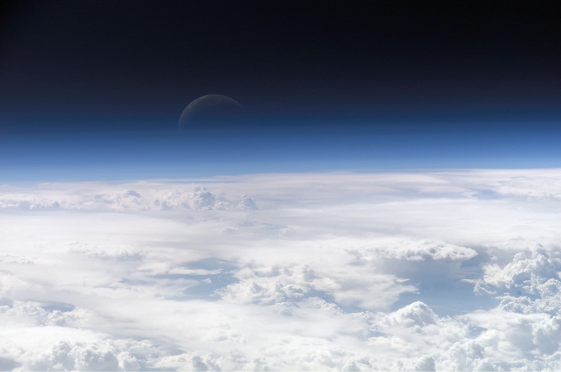 The thin blue band of Earth's atmosphere seen edge-on from orbit, the crescent moon above.