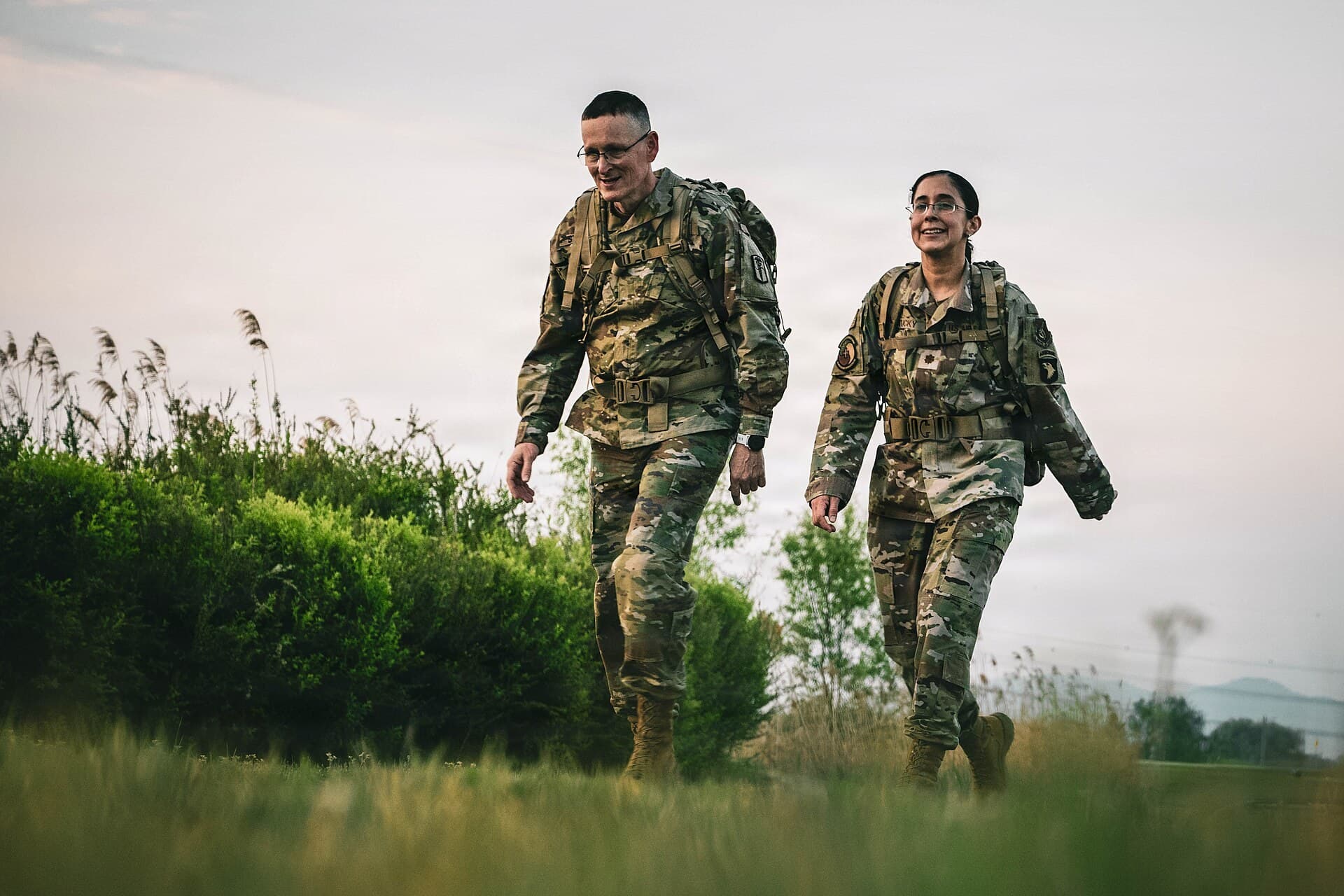 Two soldiers with packs walking through grass on the 30 km Norwegian Foot March.